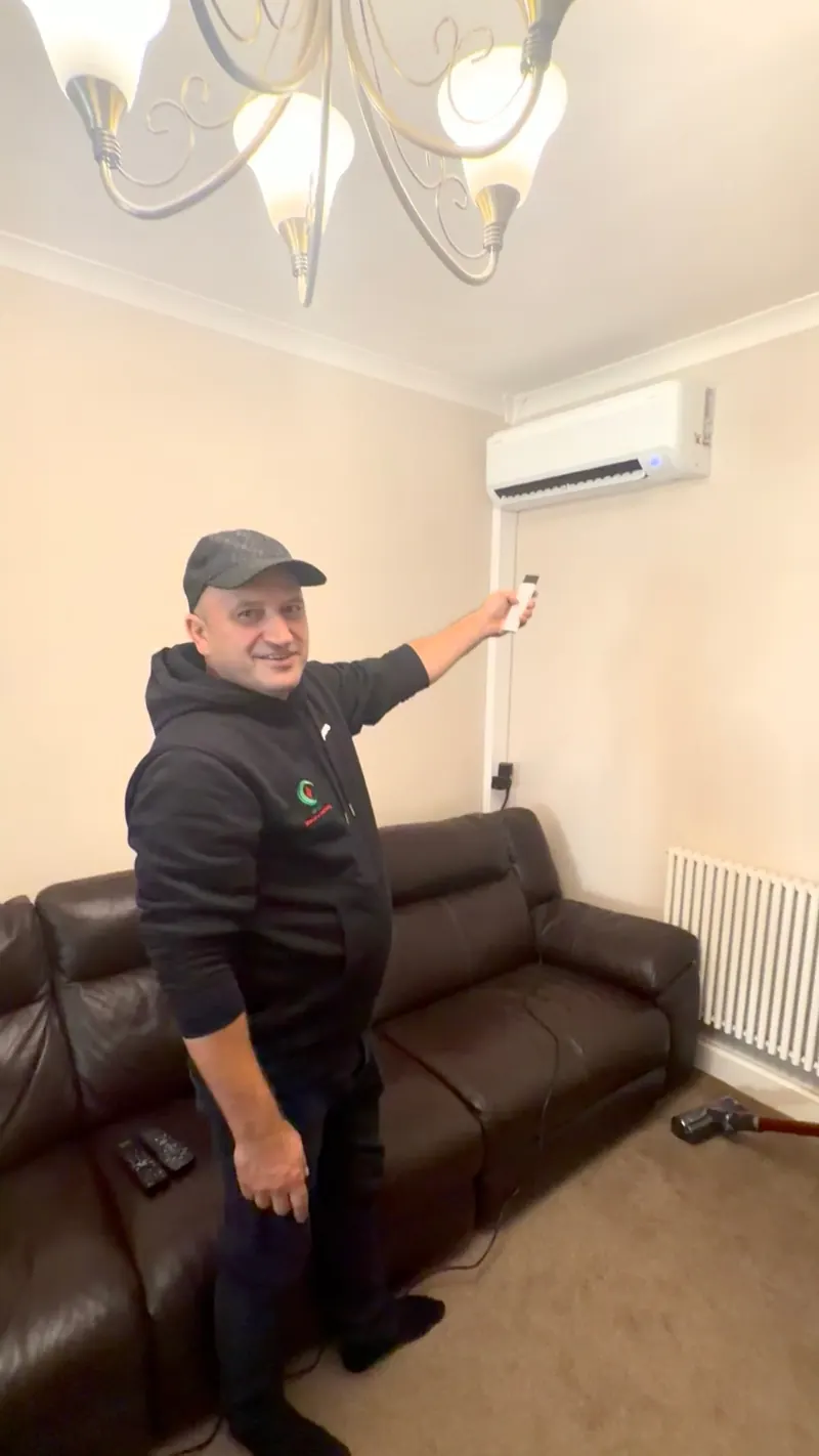 Engineer holding the controller beside a wall-mounted indoor unit above a sofa